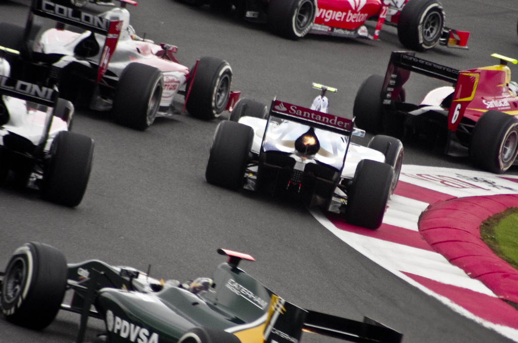 A pack of single-seater racing cars bunched together going into a corner